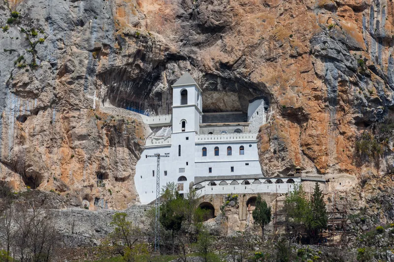 The white Upper Monastery of Ostrog set impossibly into the grey-and-orange cliff face, the cave church high above the Bjelopavlići plain