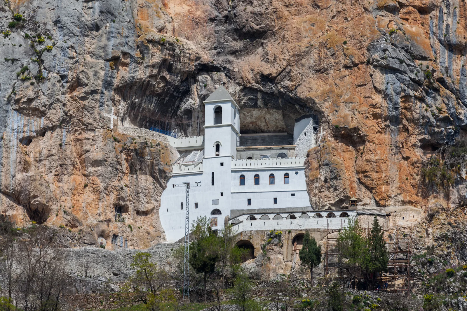 The white Upper Monastery of Ostrog set impossibly into the grey-and-orange cliff face, the cave church high above the Bjelopavlići plain