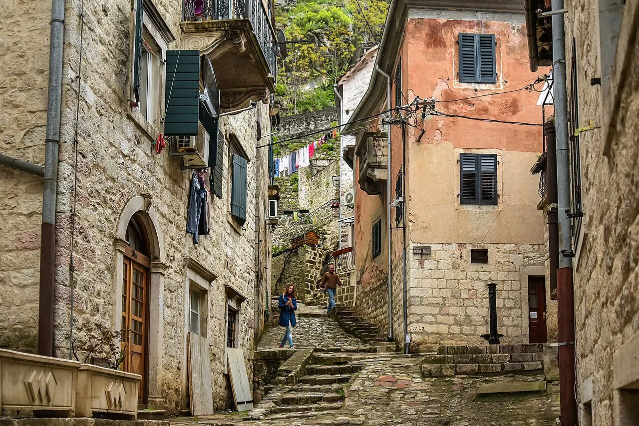 A narrow, steep cobbled stone lane and stairway rising between old stone buildings in Kotor's Old Town, uneven paving