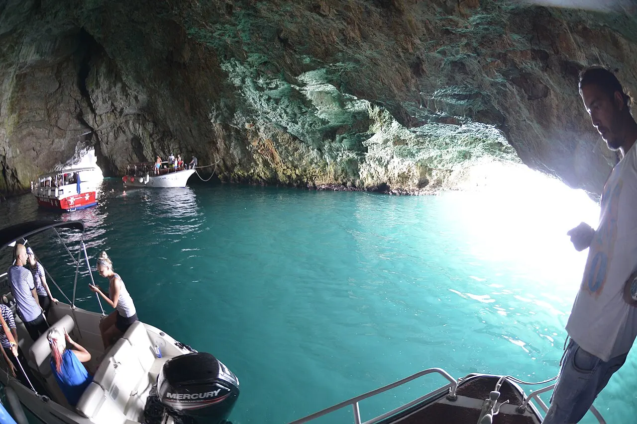 The electric-blue glowing water inside the Blue Cave (Plava spilja) near the bay's mouth, small tour boats in the grotto