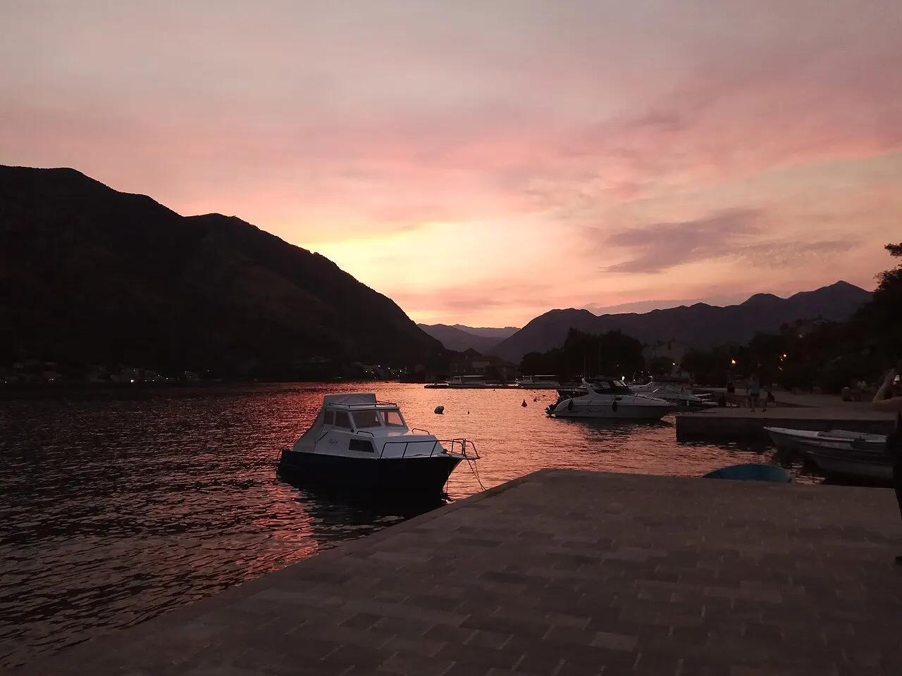 Sunset over the Bay of Kotor seen from the shore, the glowing ridgelines reflected in the calm water