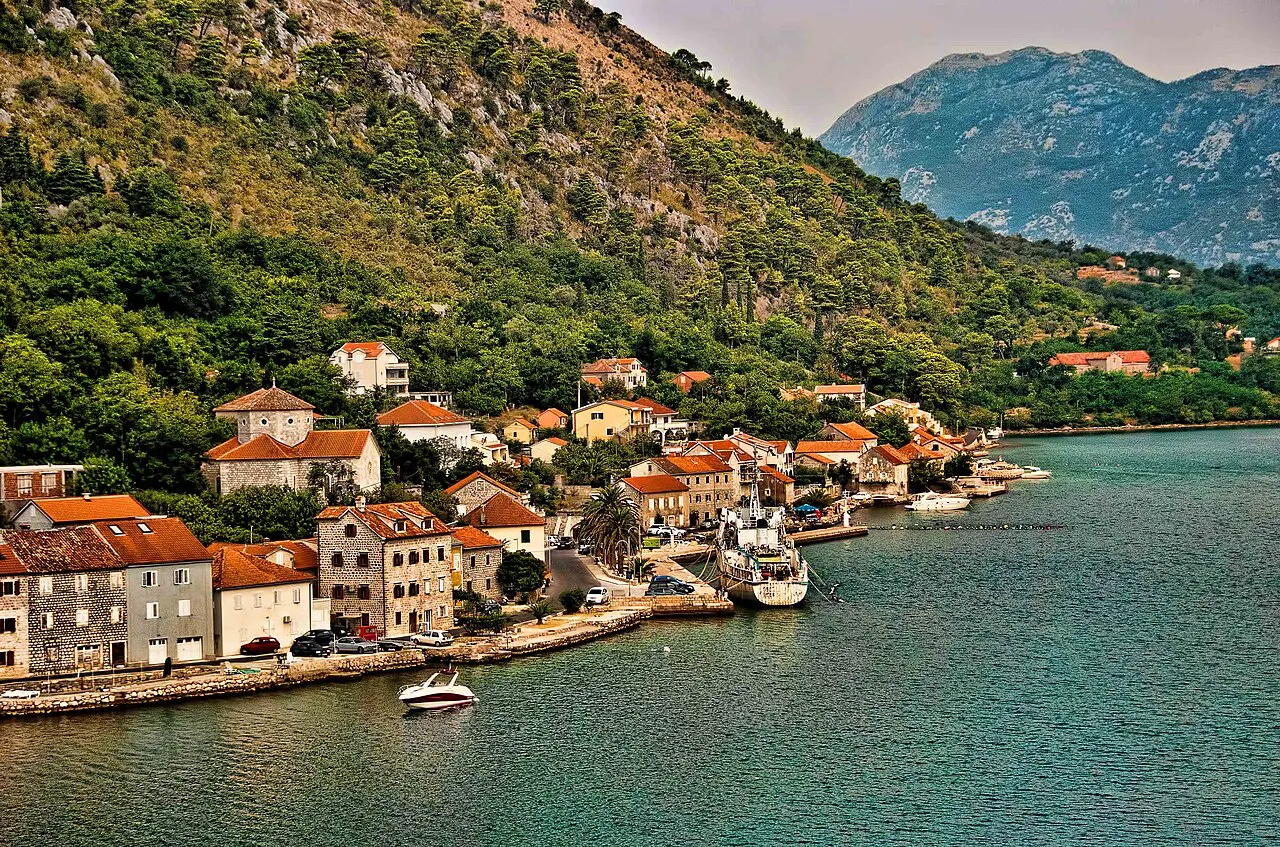 The Dobrota waterfront on the Bay of Kotor, old stone captains' houses along the calm shore with mountains beyond
