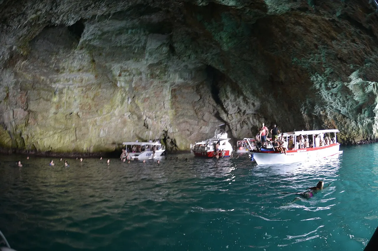 Several tour boats gathered inside the Blue Cave with swimmers in the turquoise water beneath the towering rock walls