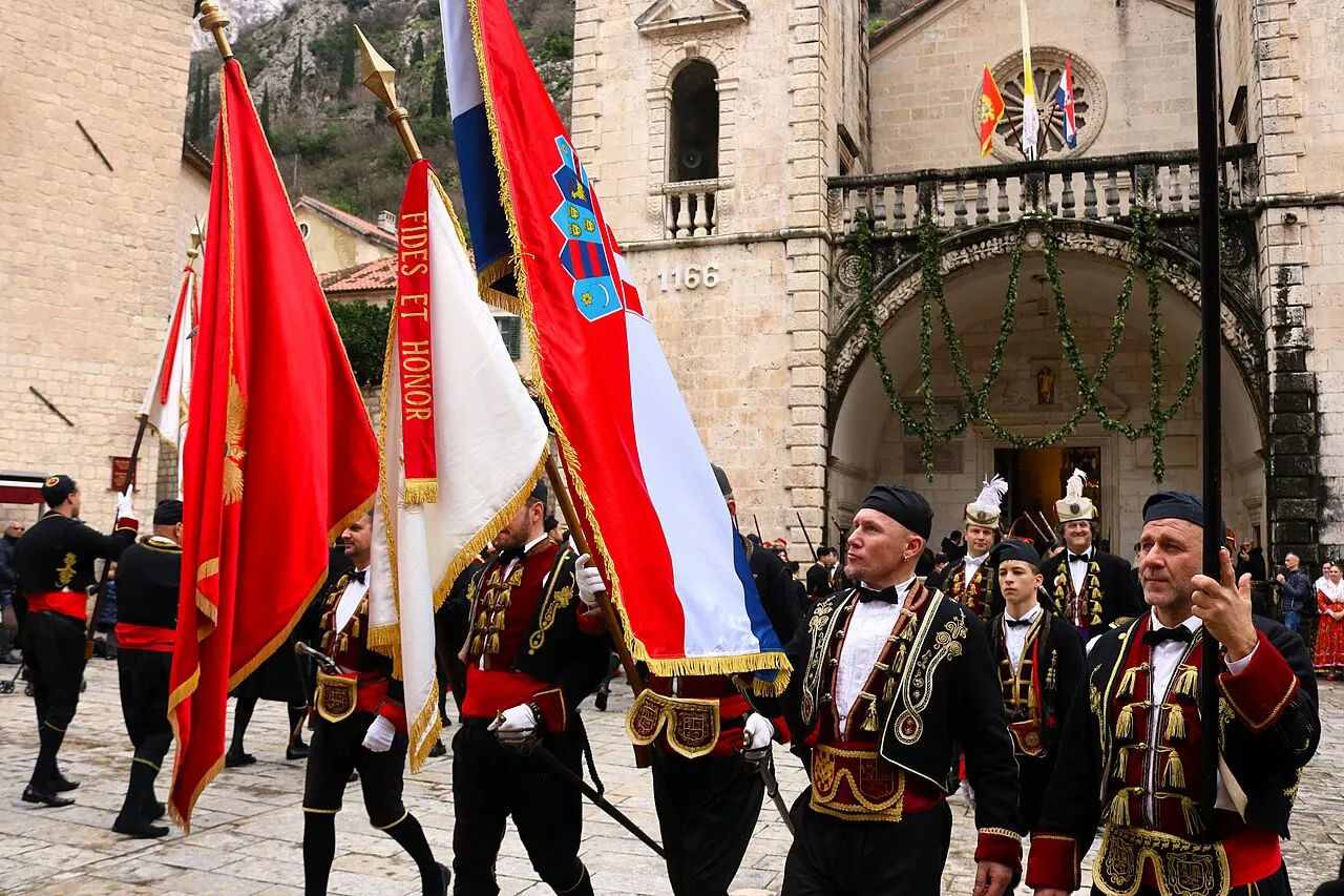 Boka Navy members in gold-braided uniform with banners before the Romanesque facade of St Tryphon Cathedral, Kotor