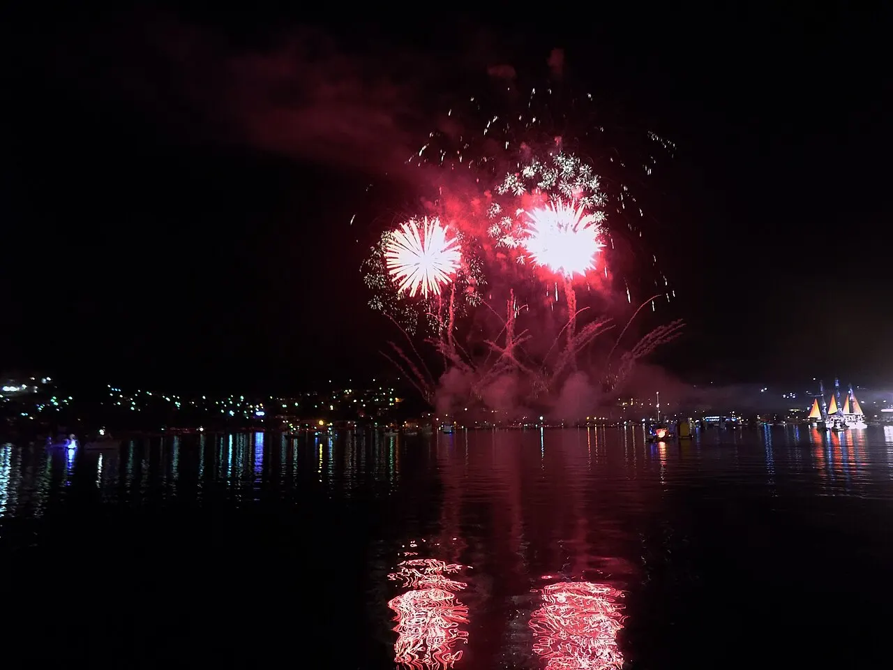 Vivid red fireworks bursting over the Bay of Kotor at the Boka Night finale, bursts and town lights reflected in water