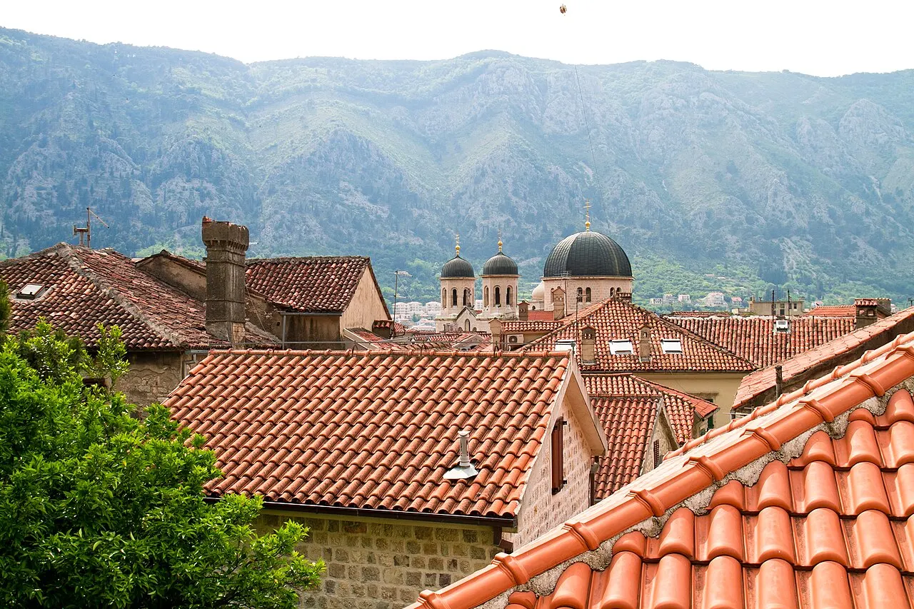 A close view across the terracotta rooftops of Kotor's Old Town with church domes and belltowers, steep mountains behind