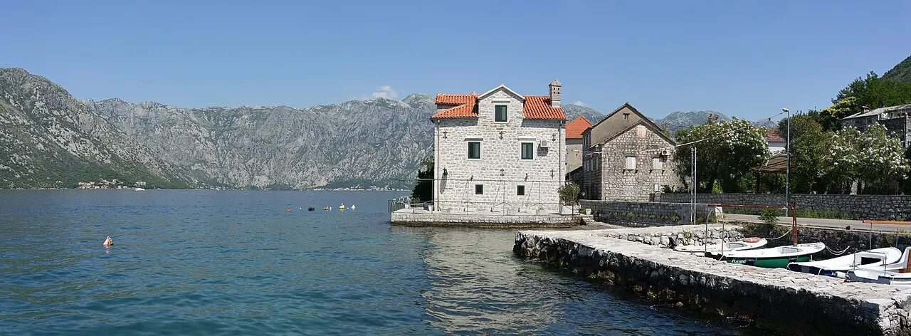 An old stone house at the water's edge in Stoliv on the Bay of Kotor, the quiet bay and far shore beyond