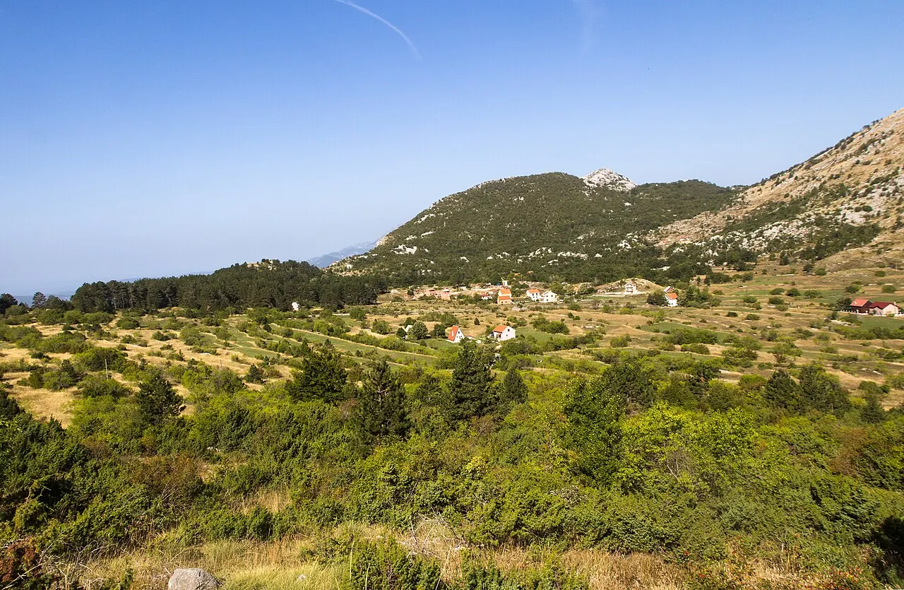 The high karst field of Lovćen National Park opening out toward a village in a valley ringed by bare karst mountains