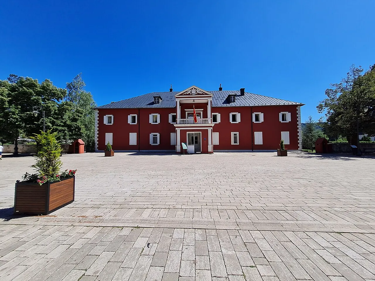 The red King Nikola Royal Palace in Cetinje, now a royal-era museum, seen across its broad stone-paved forecourt