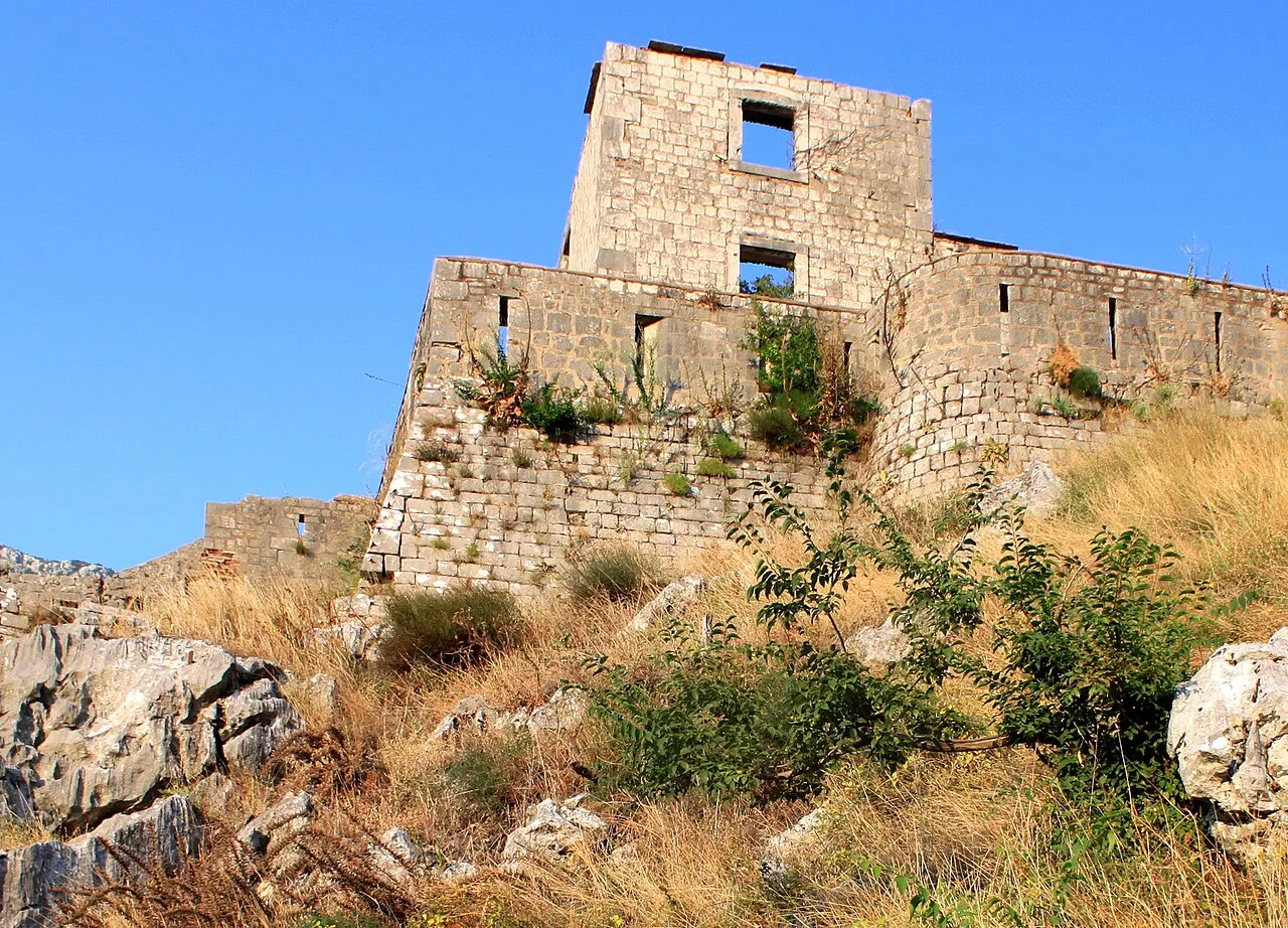 Kotor's stone fortress walls and a ruined bastion glowing in warm late-afternoon light against a deep blue sky