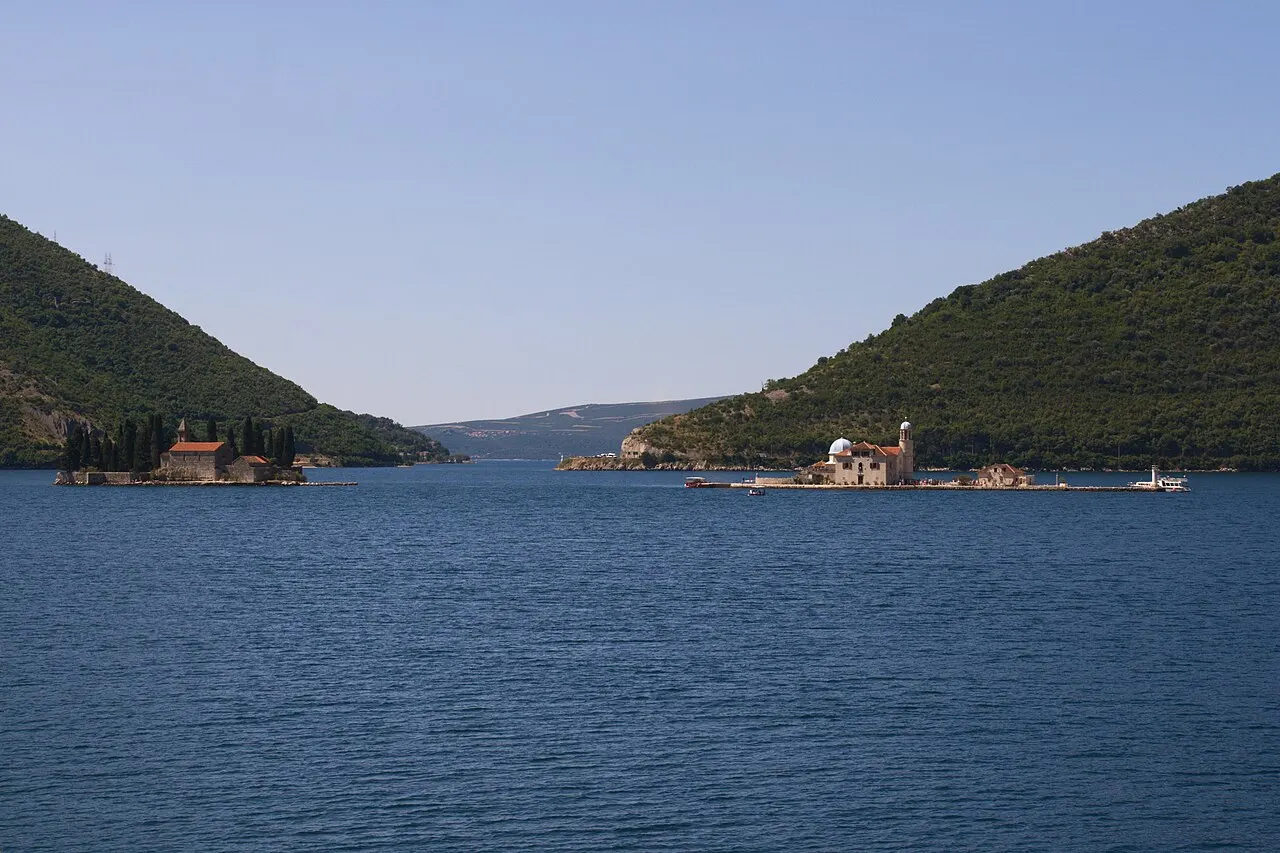 View across the glassy inner Bay of Kotor toward the islands of Sveti Đorđe and Our Lady of the Rocks ringed by mountains