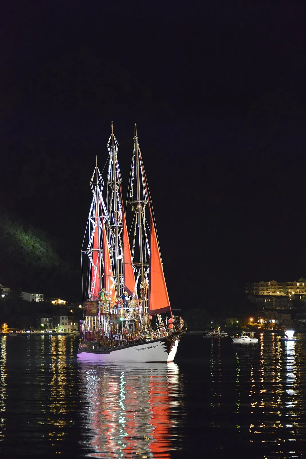 An illuminated tall ship with red sails on the Bay of Kotor at night during the Boka Night Festival