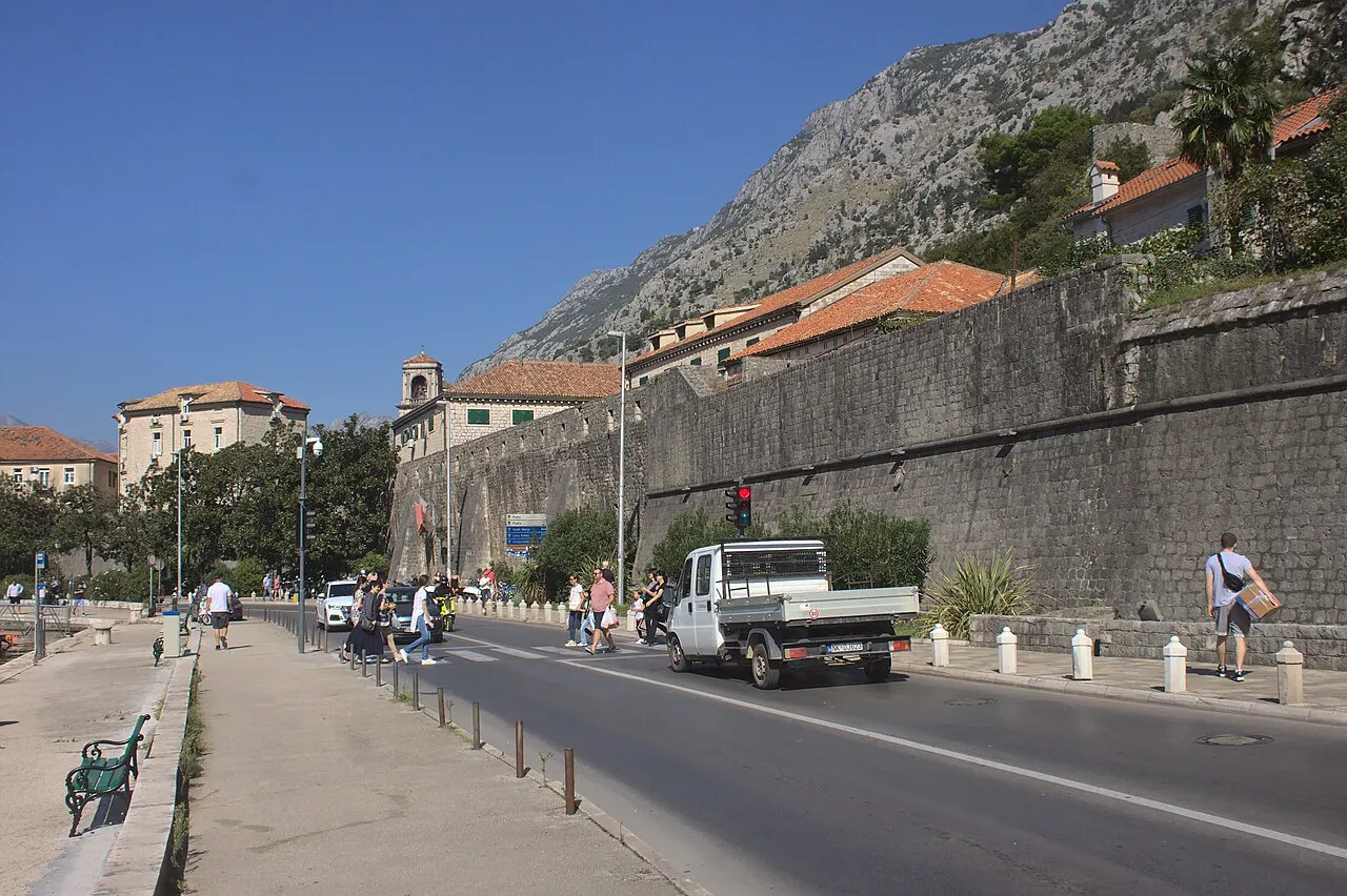 Flat road and pedestrian path running alongside Kotor's city walls, mountains rising above