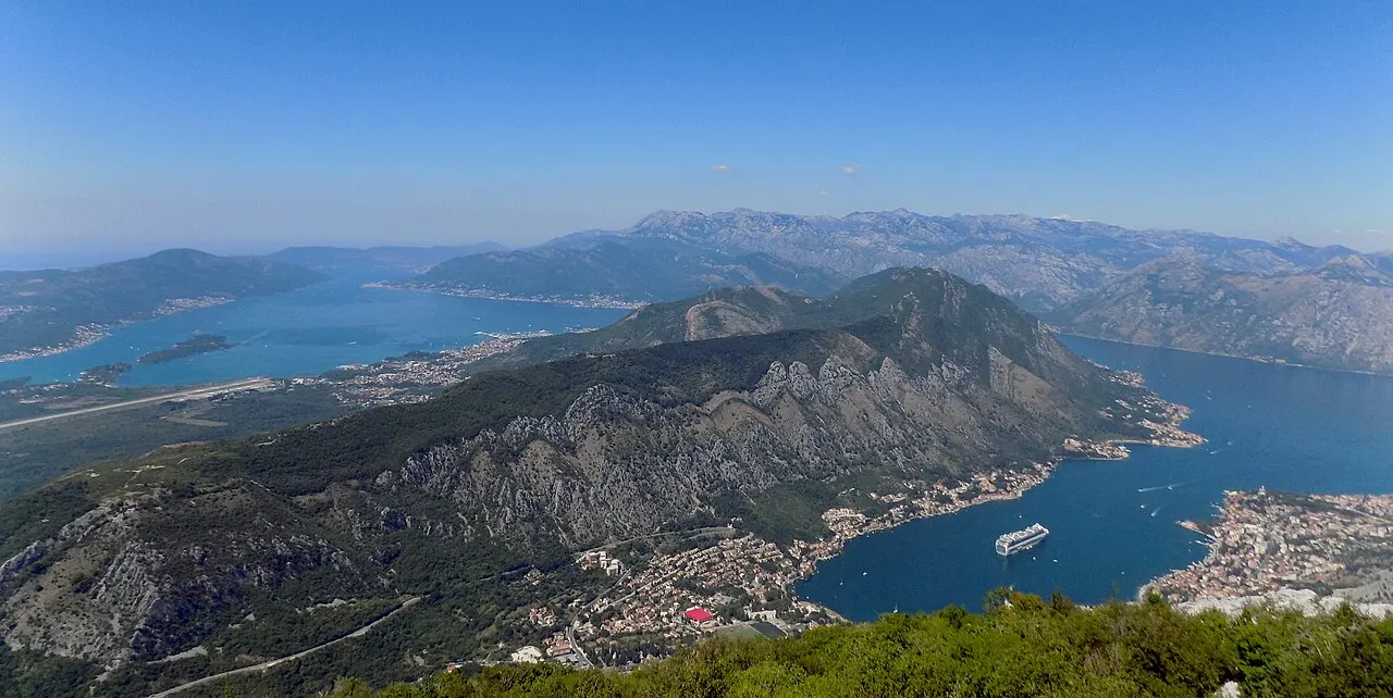 A cruise ship on the Bay of Kotor below the mountains, the walled town and quay alongside