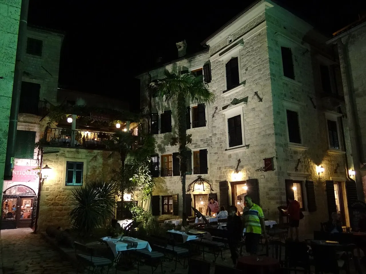 A lamplit cafe and lane in Kotor's Old Town at night, the bay quiet after dark