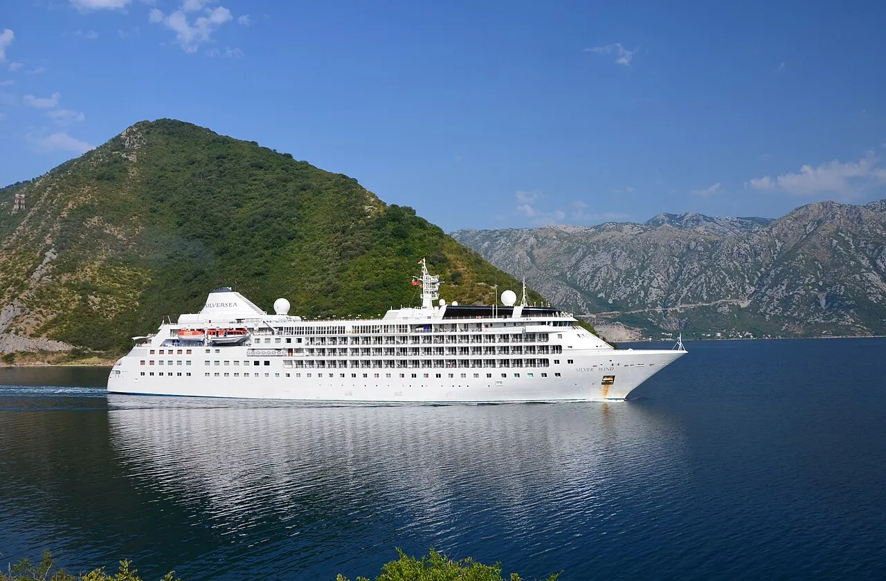 A small cruise ship on the clear water of the Bay of Kotor beneath steep green mountains
