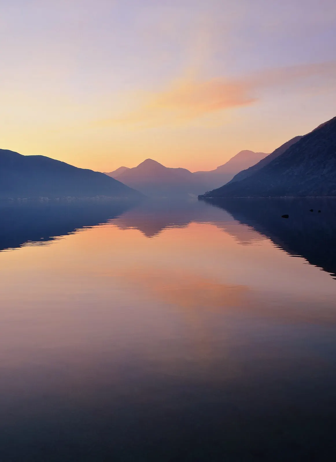Golden-hour light over the glassy inner Bay of Kotor seen from Ljuta village, mountains reflected in the water