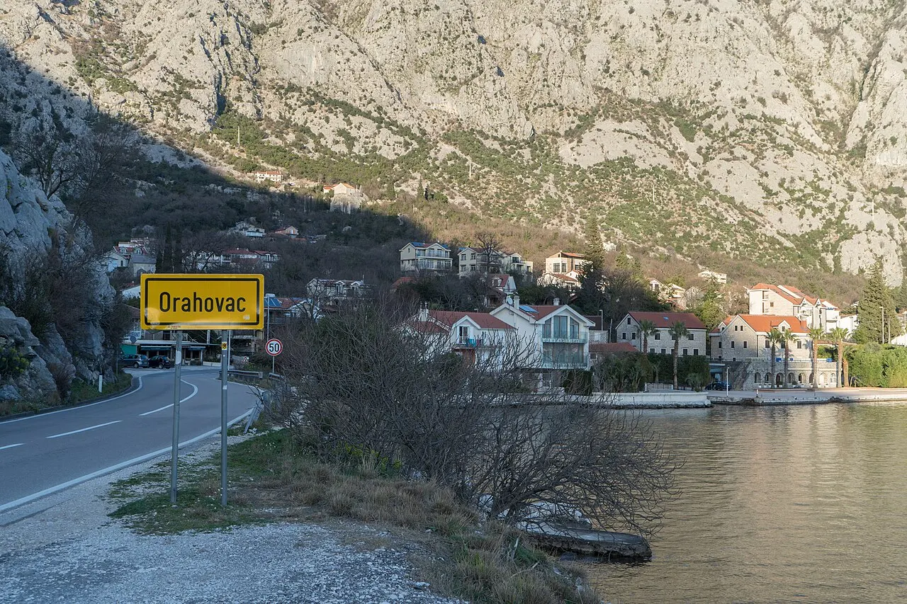A quiet waterfront road at Orahovac on the Bay of Kotor, village sign, stone houses and the water alongside