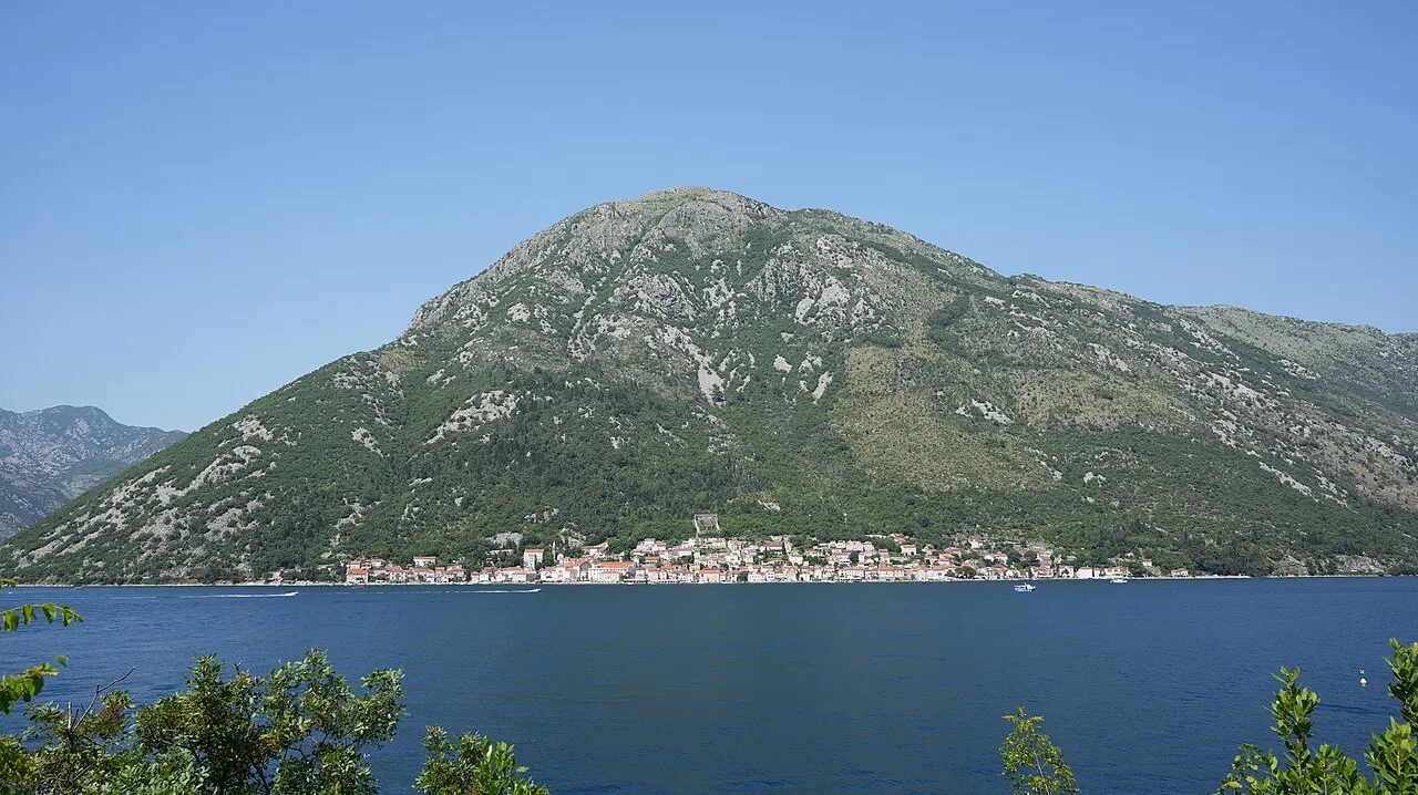 Perast spread along the calm Bay of Kotor shore beneath a steep mountain, seen across the water