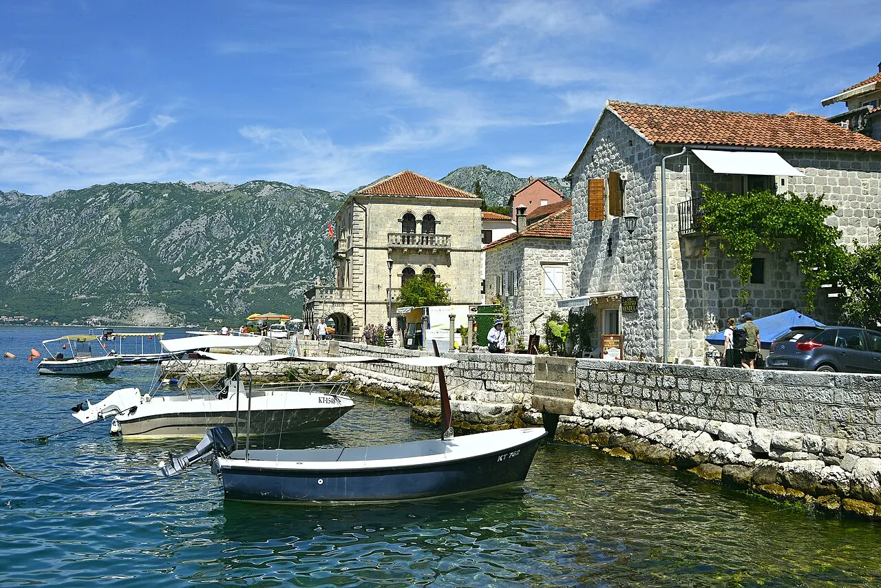 Small boats moored at the Perast waterfront below stone houses and the bay mountains