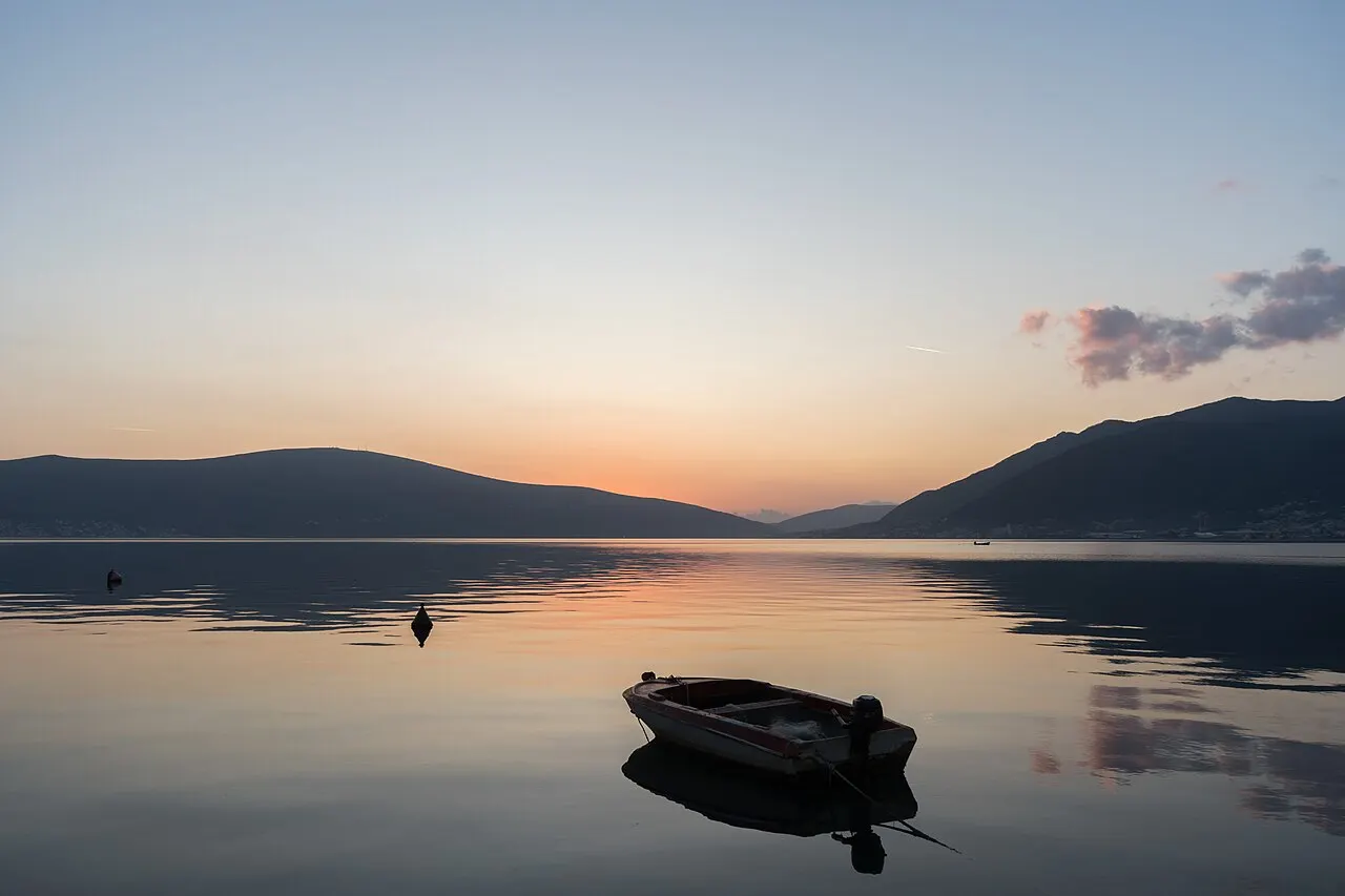 A quiet waterfront in Donja Lastva on the Bay of Kotor at dusk, boats on the still water below the mountains