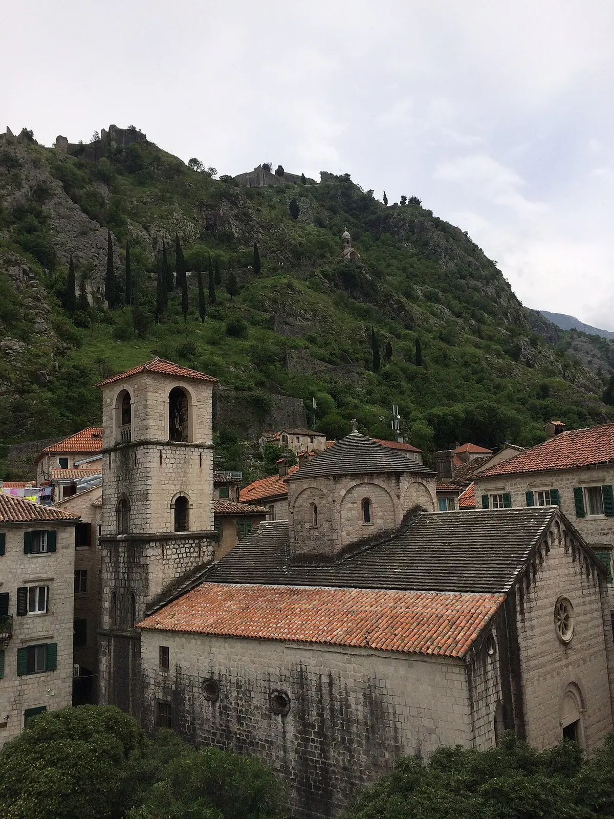 Romanesque belltowers and terracotta rooftops in Kotor's walled Old Town, the fortification walls on the hill behind